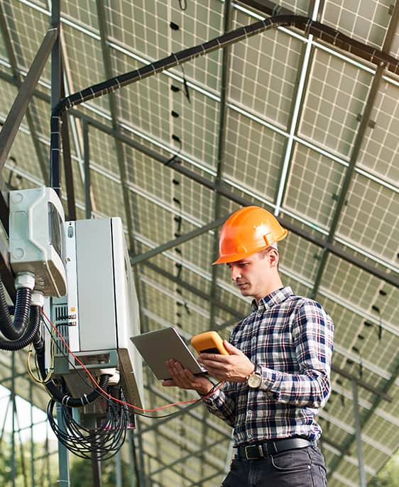 A man in a hard hat and plaid shirt poses in front of a solar panel.