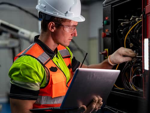 A construction worker in a hard hat and safety vest is using a laptop to complete tasks on-site.