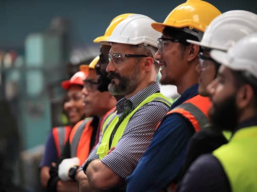 A group of men in hard hats and safety vests, standing together at a construction site.