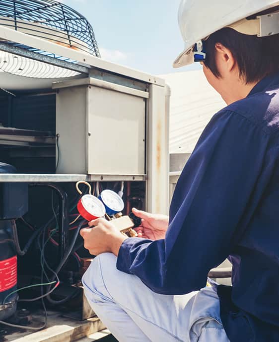 A man in a hard hat and white shirt repairs an air conditioner.