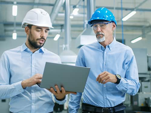 Two men in hard hats standing side by side, engaged in conversation at a construction site.