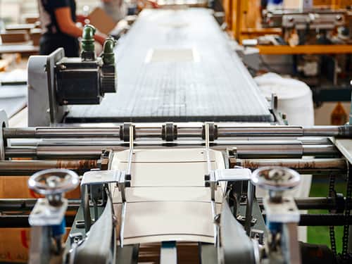 A large machine operates in a factory, producing sheets of paper in a continuous manufacturing process.