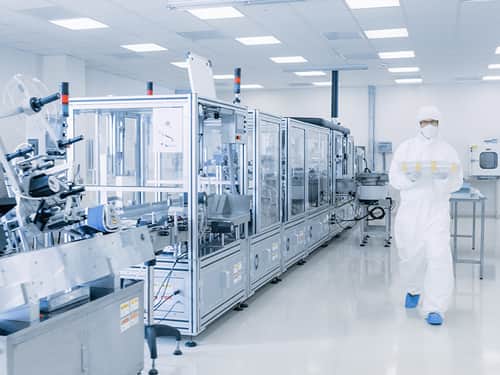 A man in a white lab coat stands beside a large machine in a laboratory setting.