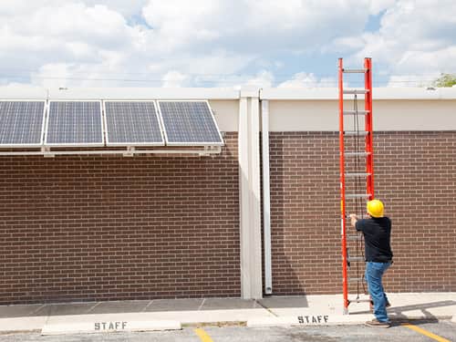 A man is positioned on a ladder next to a building, engaged in tasks related to its upkeep or repair.