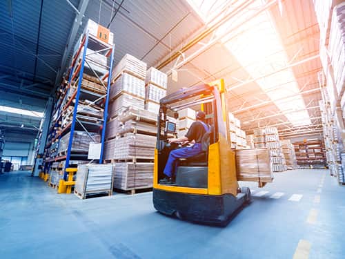 A forklift truck navigating through a spacious warehouse filled with shelves and stacked goods.