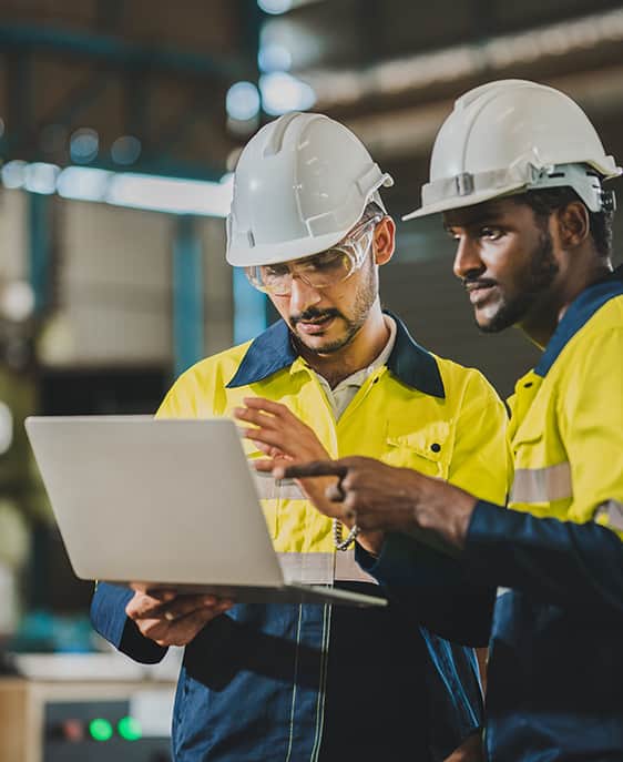 Two men in hard hats examining a laptop, engaged in a discussion about their work project.