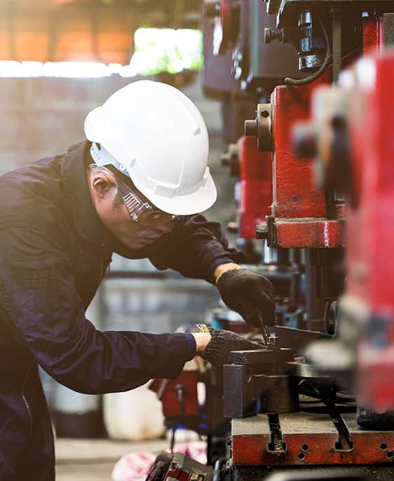 A man operates a machine in a factory, focused on his task amidst industrial equipment and surroundings.