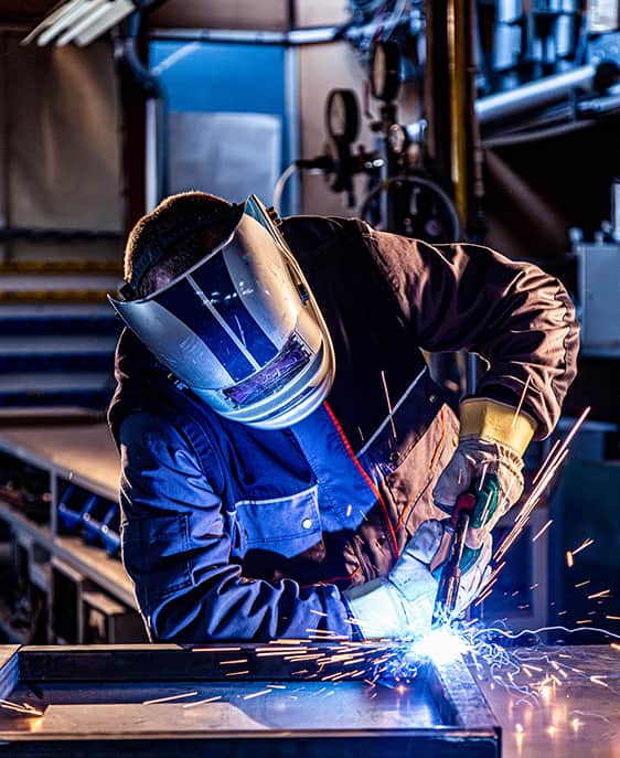 A man in a welding helmet is engaged in metalwork.