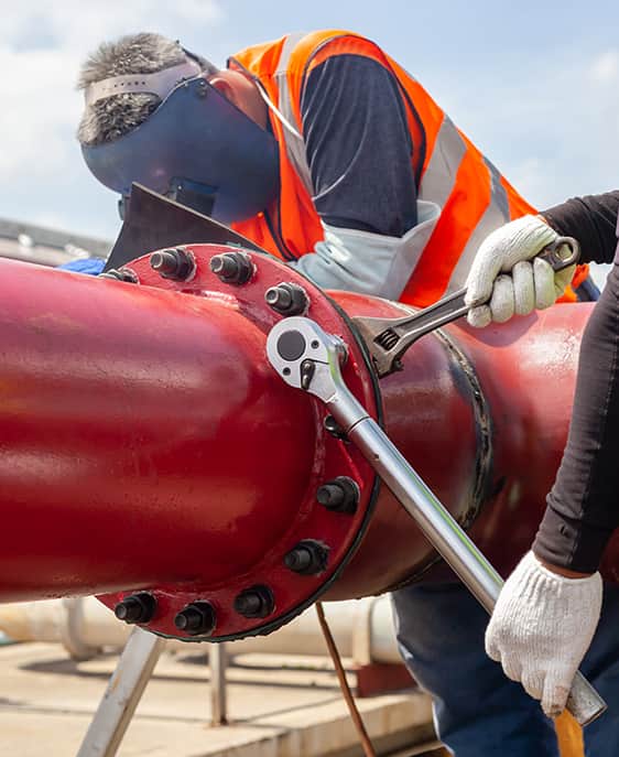 Two men wearing safety vests and hard hats stand side by side, engaged in conversation at a construction site.
